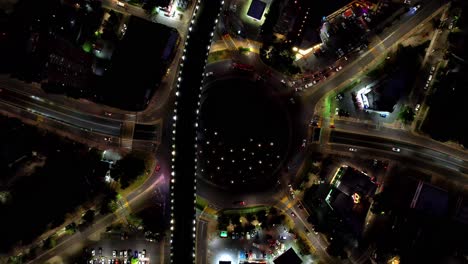 Luftbild-Von-Oben-Nach-Unten-Auf-Einen-Großen-Kreisverkehr-Mit-Brücke-Darüber-Bei-Nacht-Mit-Den-Lichtern-Einer-Großstadt