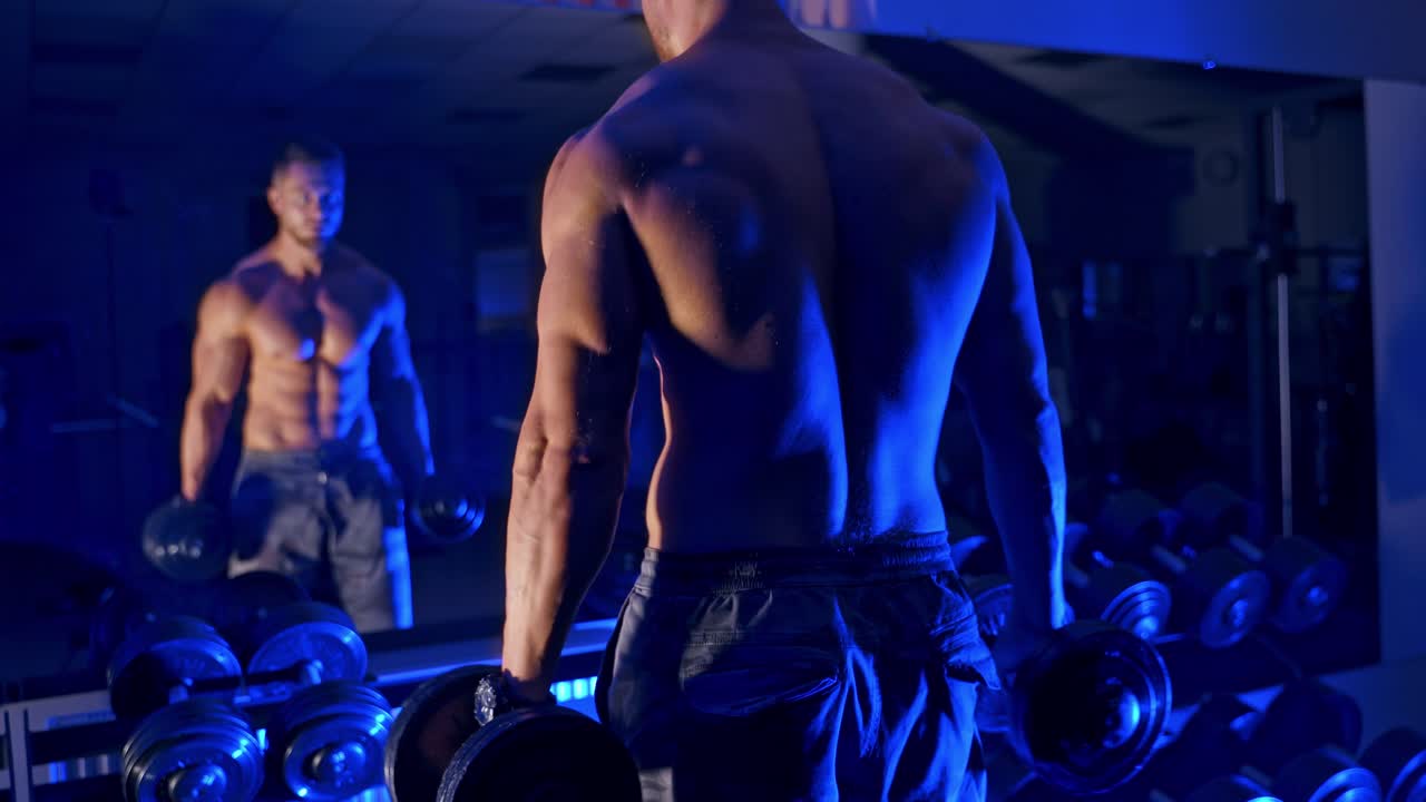 Man trains in the gym. Athletic man trains with dumbbells pumping his biceps