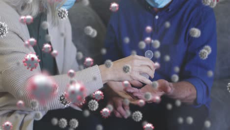 animation of virus cells over senior caucasian couple disinfecting hands with face masks