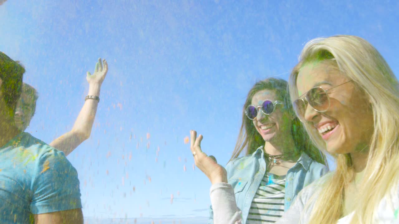 un grupo multiétnico de jóvenes diversos salta y lanza polvo de colores en el aire en la celebración del festival de holi. se divierten enormemente en este día soleado.