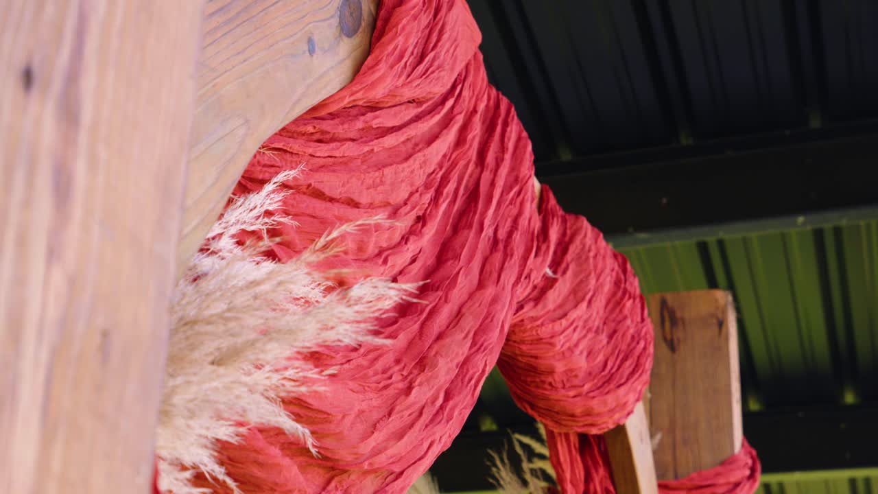 Detailed close-up shot of a rustic wedding arch, highlighting flowing fabric and natural floral elements under the venue's canopy.