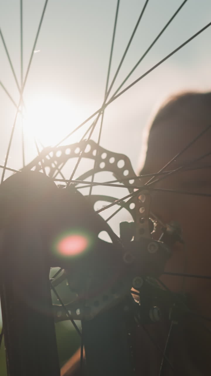 dama tocando suavemente la rueda de la bicicleta con una cálida sonrisa mientras la luz del sol se refleja en ella y la rueda giratoria, creando un momento mágico, el fondo borroso añade a la serenidad