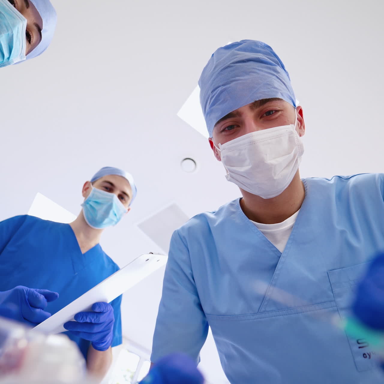 Portrait of a young doctor with syringe. Three specialists in masks giving resuscitation to a patient. Working process of medical group in the emergency room.