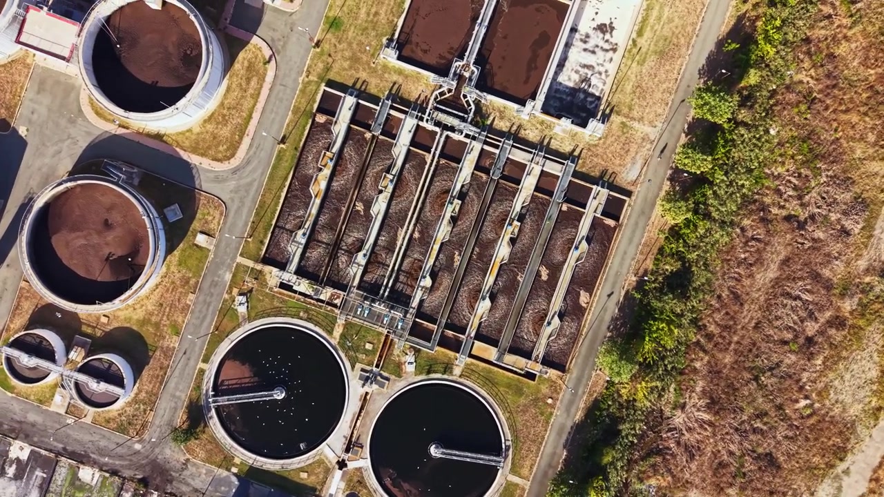 Wastewater treatment plant seen from above showing several tanks and processing areas with various stages of water treatment
