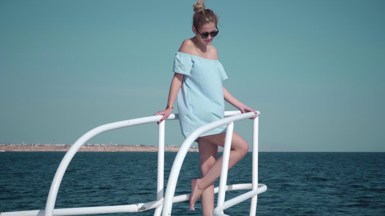 파란색 드레스와 선글라스를 입고 요트에 탑승한 젊은 섹시한 카우카스 여성의 초상화 - 휴가, 자유, 빛 여름의 개념 - 배경에 파란 바다
