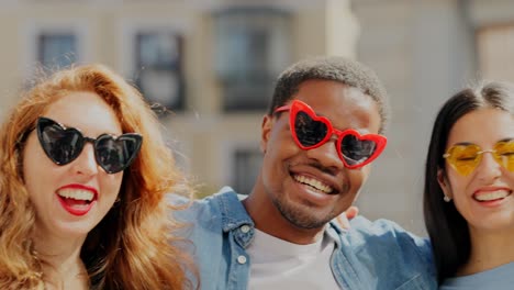 a happy diverse group of friends wearing heart-shaped sunglasses laughing outdoors