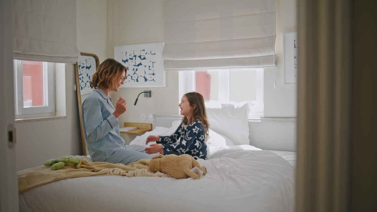 Pyjamas family enjoying morning at white bedroom. Mom daughter playing at bed