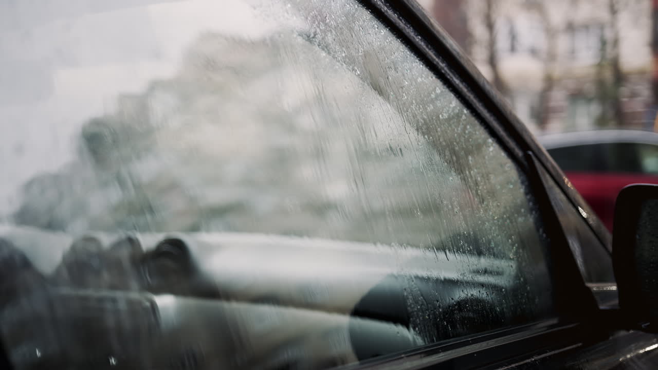 Primo piano di gocce di pioggia che coprono il finestrino dell'auto con sfondo urbano sfocato
