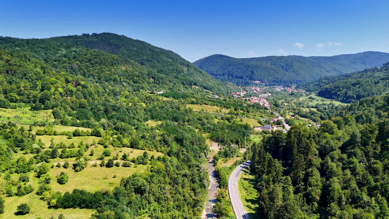 Scenic mountain valley with village and river below. Aerial view of small Romanian village surrounded by green forests and river flowing through valley