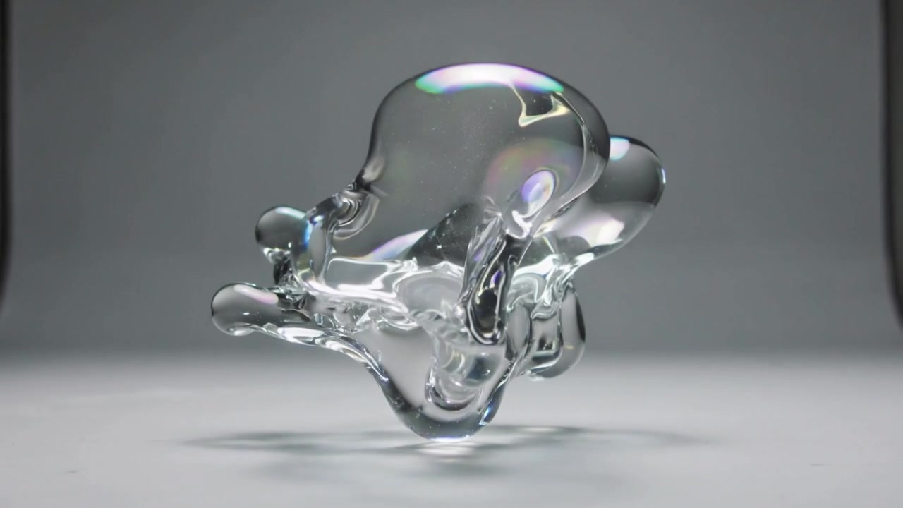 Emerging clear glass-like droplet expanding, reshaping, rotating over gray stage for lighting study