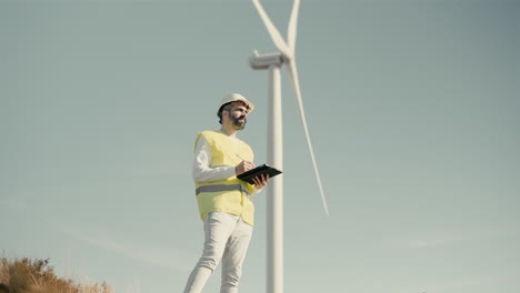 eco-conscious engineer checks wind turbines in a field of renewable energy generators, using technology on tablet to ensure a sustainable future