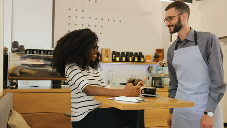 young caucasian waiter bringing a cup of coffee to the young african woman in a coffee shop