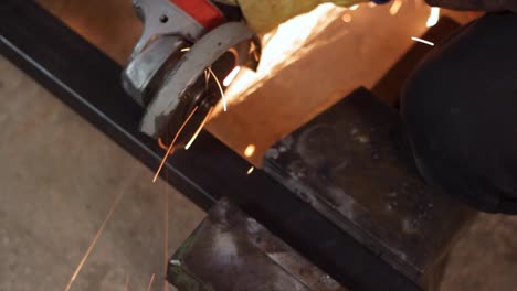 hand worker cutting piece of black square metal bar, close high angle