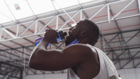 African-american-man-wearing-lowered-face-mask-drinking-at-gym