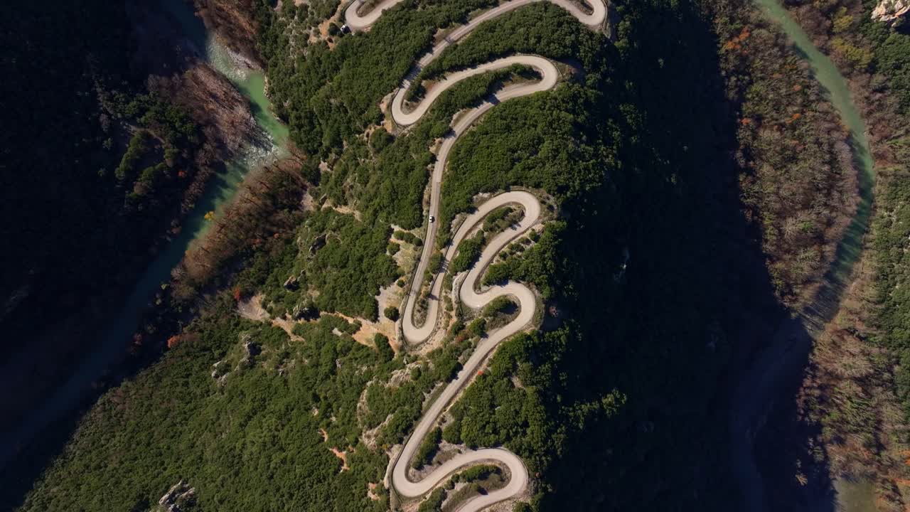 Drone view of vehicles on rugged road framed by autumn trees