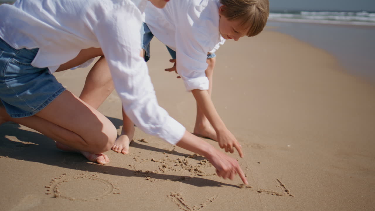Mother son drawing sand enjoying sea vacation together closeup. Smiling mom boy