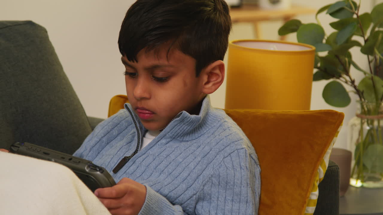 Young Boy Sitting On Sofa At Home Playing Game Or Streaming Onto Handheld Gaming Device 4