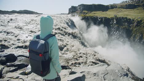 woman standing at the cliff edge looking at detifoss waterfall in iceland