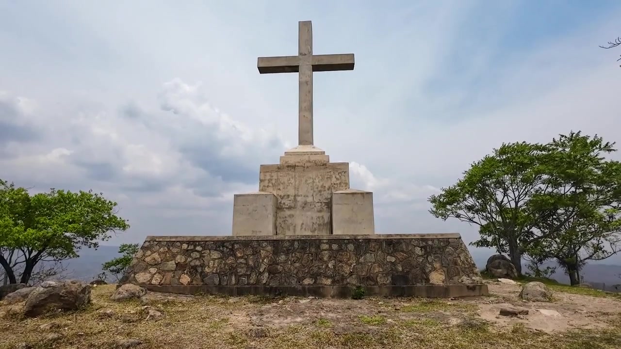 Una panorámica vertical revela el monumento del Vía Crucis en la cima de la colina entre dos árboles contra un cielo blanco y azul en el Monte Michiru en Blantyre, Malawi