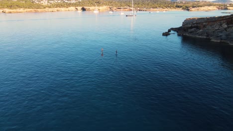 Luftaufnahme-Hinter-Zwei-Menschen,-Die-Auf-Elektrischen-Surfbrettern-über-Die-Gewässer-Vor-Der-Küste-Von-Cala-Escondida-Surfen,-Kamerafahrt