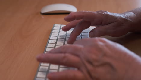 manos de una anciana escribiendo en un teclado de computadora blanco en el escritorio de la oficina