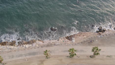 Aerial-view-looking-straight-down-onto-crashing-waves-hitting-a-grey-beach