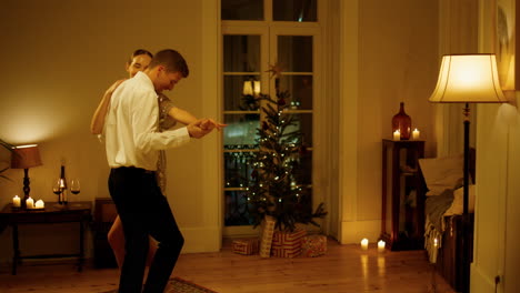 los amantes felices bailan sensualmente en un apartamento acogedor. la pareja se mueve en el interior del árbol de navidad.