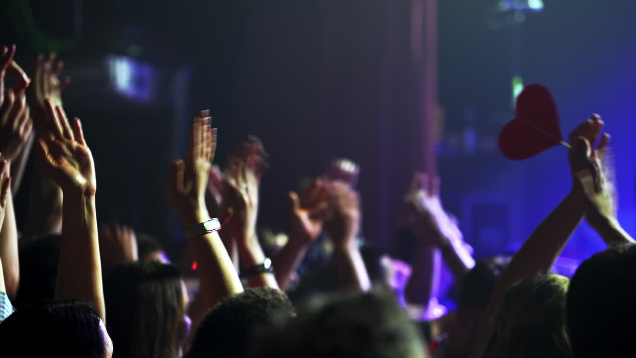 Enthusiastic fans are cheering and raising their hands, holding a red heart, expressing their love and support for the artist during a live concert