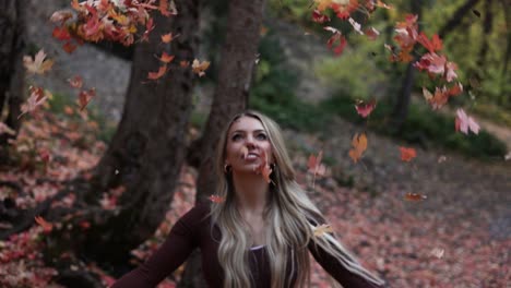 cámara lenta de una joven feliz lanzando hojas de otoño al aire