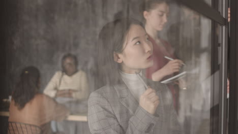 pensive asian businesswoman behind glass wall