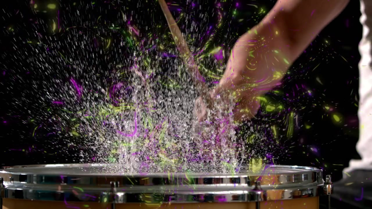 Baterista masculino golpeando la caja sobre negro, generando espirales de tiza moradas o doradas, luego preparándose para la música