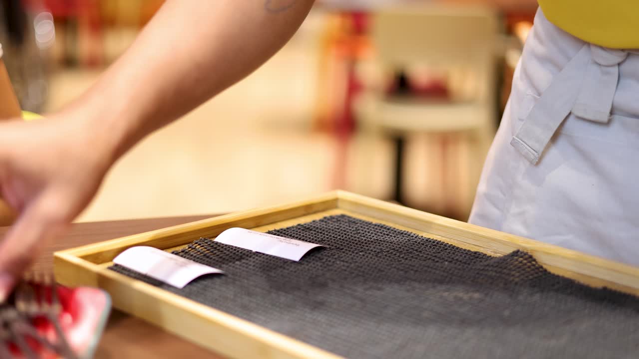 A server in casual attire places a lemon soda, straws, and napkins on a wooden tray at a restaurant table under warm indoor lighting