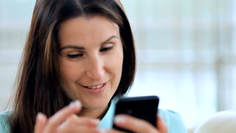 joven feliz usando su teléfono inteligente en el sofá en el interior