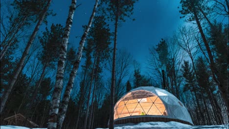 a timelapse shot outside on a beautiful winters night with a view of a geodesic airbnb accommodation in the wilderness surrounded by trees and stars in the background shot in 4k