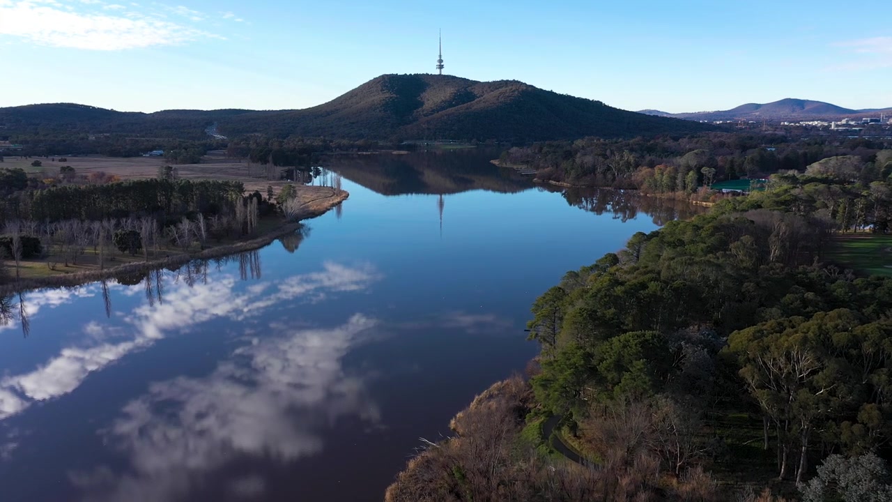 Upea ilmakuva Canberran Burley Griffin -järvestä etenee, pilvien ja Telstra Towerin heijastuessa vedessä.