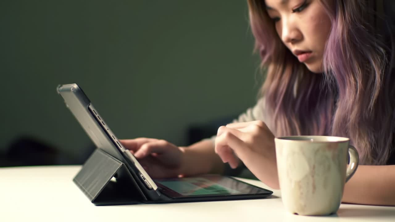 Focused Engagement: A Young Woman Utilizing Her Tablet While Enjoying a Warm Drink, Capturing a Moment of Concentration and Serenity in a Cozy Environment