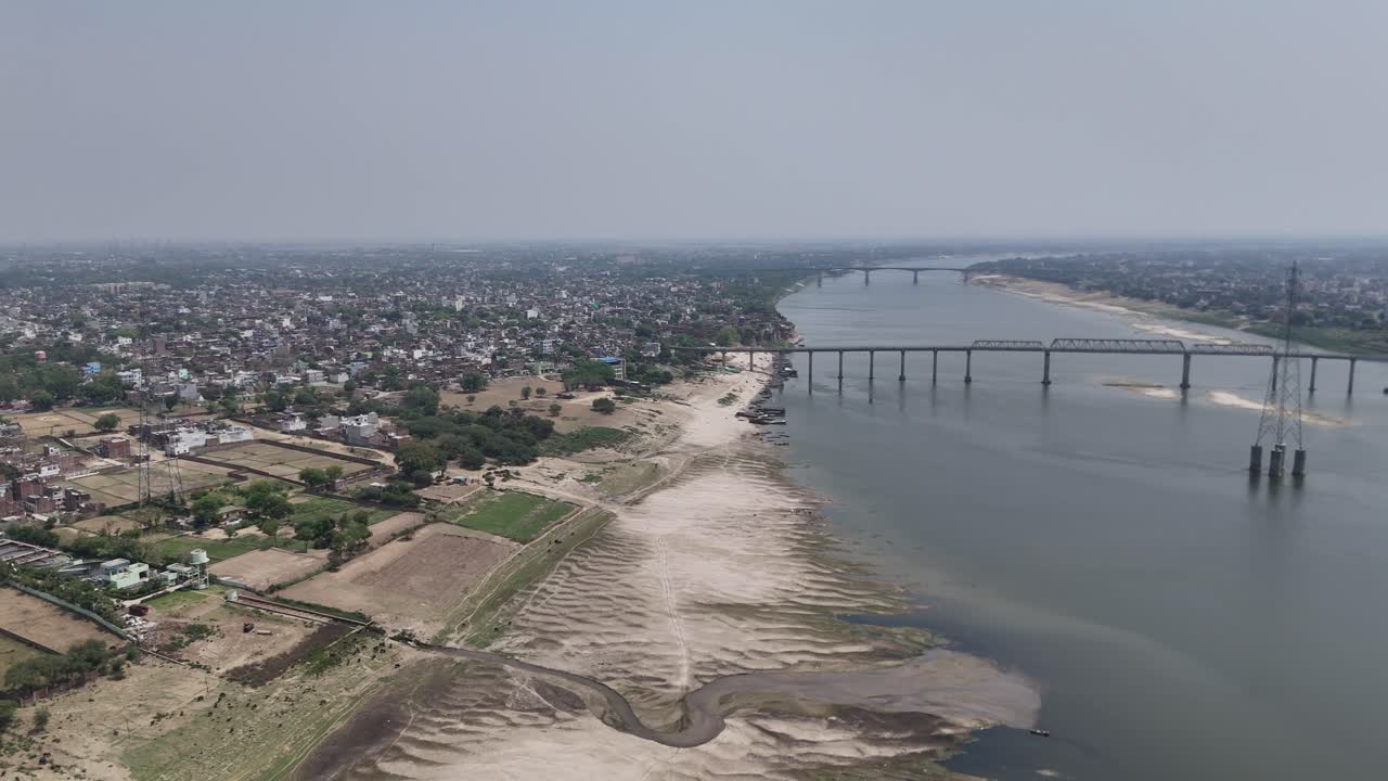 Overhead perspective of the Ganges River as it curves past the sandy banks and crowded ghats of Varanasi, a city that breathes with the pulse of ancient India.