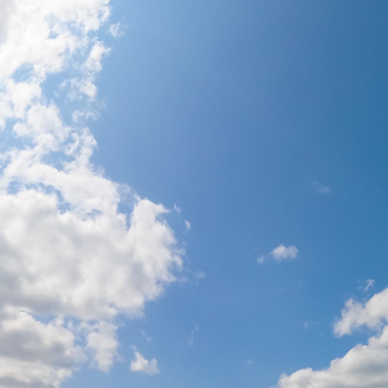 Light blue summer sky with occasional white clouds appearing and transforming. Bright sun shining on the cloudscape. Low angle view timelapse