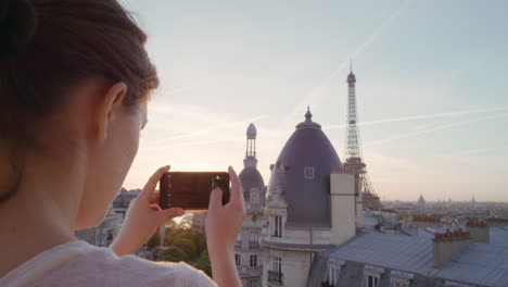 mujer feliz usando un teléfono inteligente tomando fotos disfrutando de compartir la experiencia de las vacaciones de verano en parís fotografiando una hermosa puesta de sol vista de la torre eiffel en el balcón de cerca