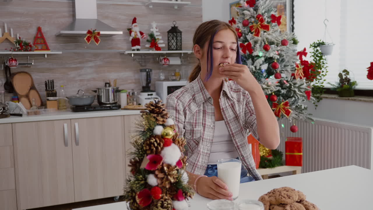 niño sentado en la mesa en la cocina decorada comiendo galletas horneadas tradicionales de navidad bebiendo leche