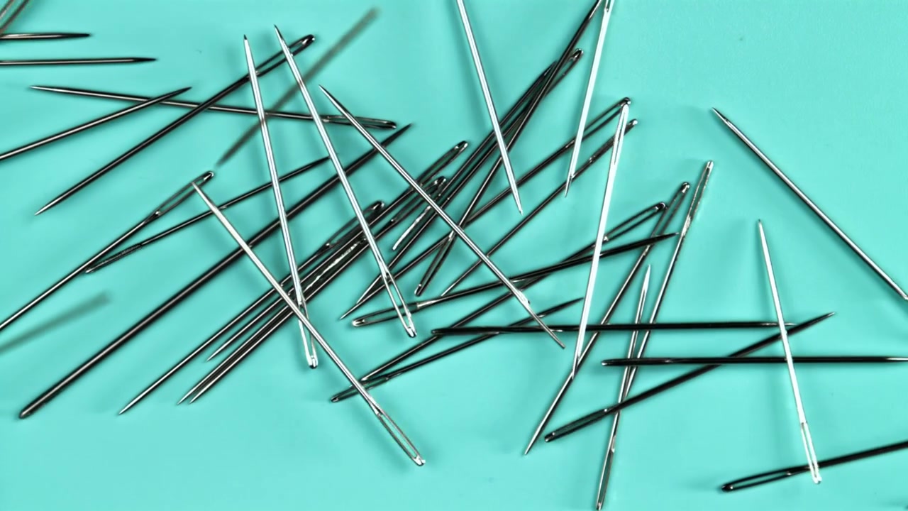 Metallic Sewing Needles Falling onto a Bright Turquoise Surface