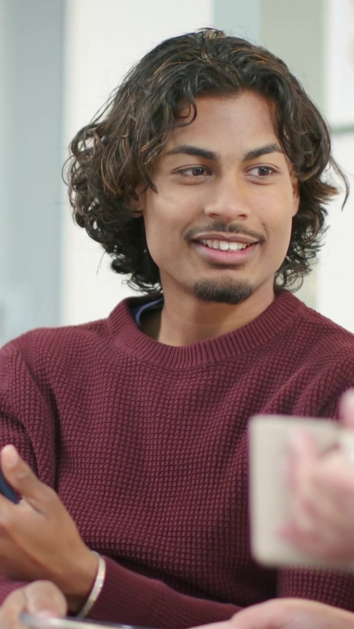 Video verticale: Uomo con maglione bordeaux che usa un telefono blu per condividere un video con un amico sul divano, popcorn