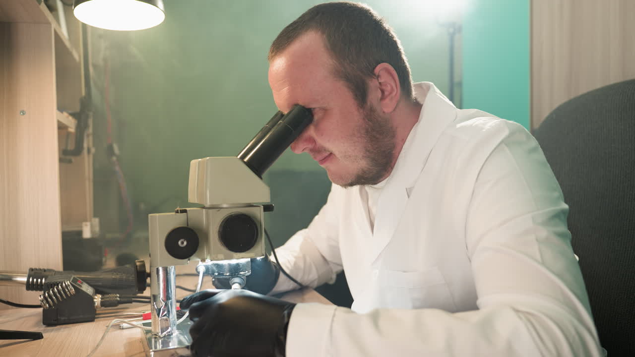 A close-up view of a dedicated technician in a lab coat, intensely working on an electronic circuit board under a microscope