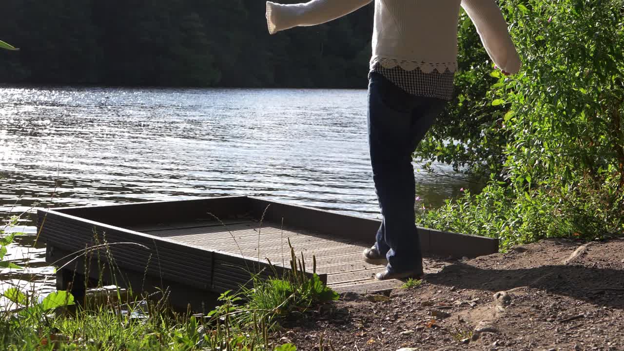 Donna in solitudine cammina sul molo di un lago, inquadratura ampia