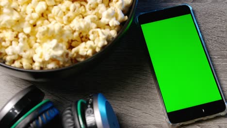 teléfono inteligente con pantalla táctil verde y palomitas de maíz en un cuenco grande en la mesa.