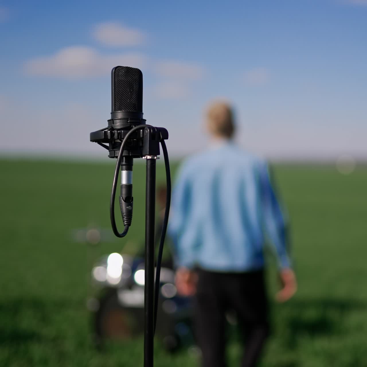 Modern professional microphone on the stand in the nature outdoors. Close up. Lead singer and his band playing music at backdrop in blur in the field