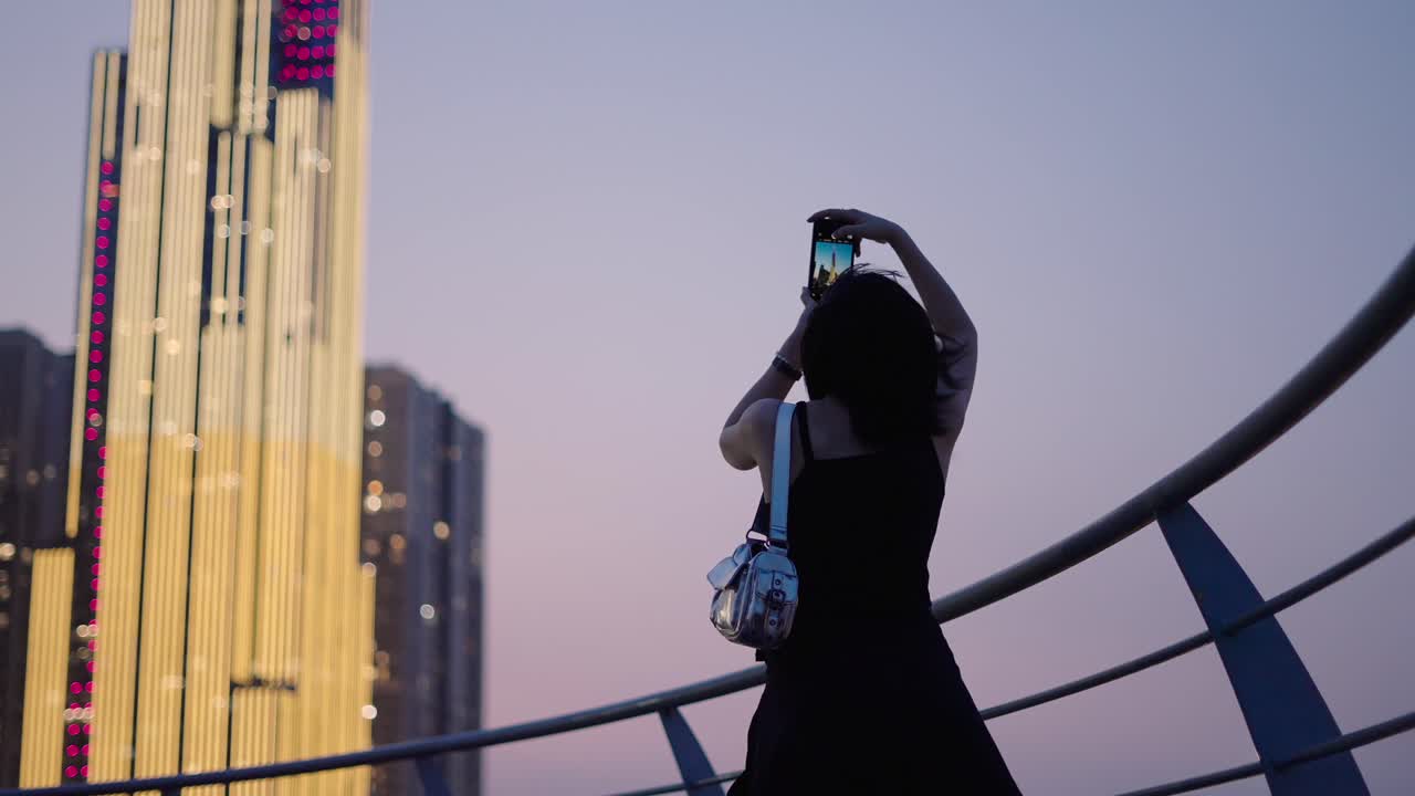 Woman taking photo of illuminated skyscraper at dusk in city