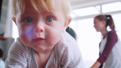 White-toddler-crawling-to-camera,-women-and-toddlers-behind