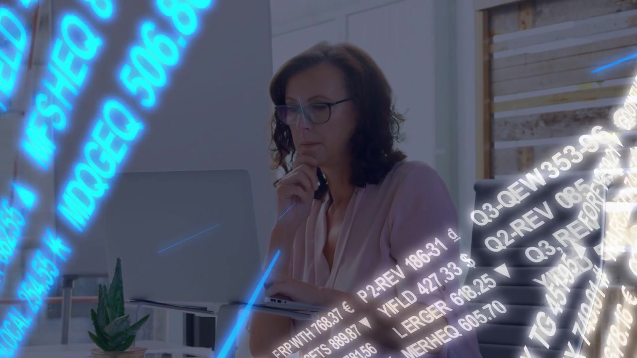Una donna matura digita al portatile in ufficio, causando lo scorrere di frecce di un ticker finanziario in movimento per i dati di mercato.