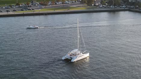 Catamaran-Boat-Sailing-At-Lake-Pontchartrain-With-Traffic-On-Lakeshore-Drive-In-Louisiana,-USA